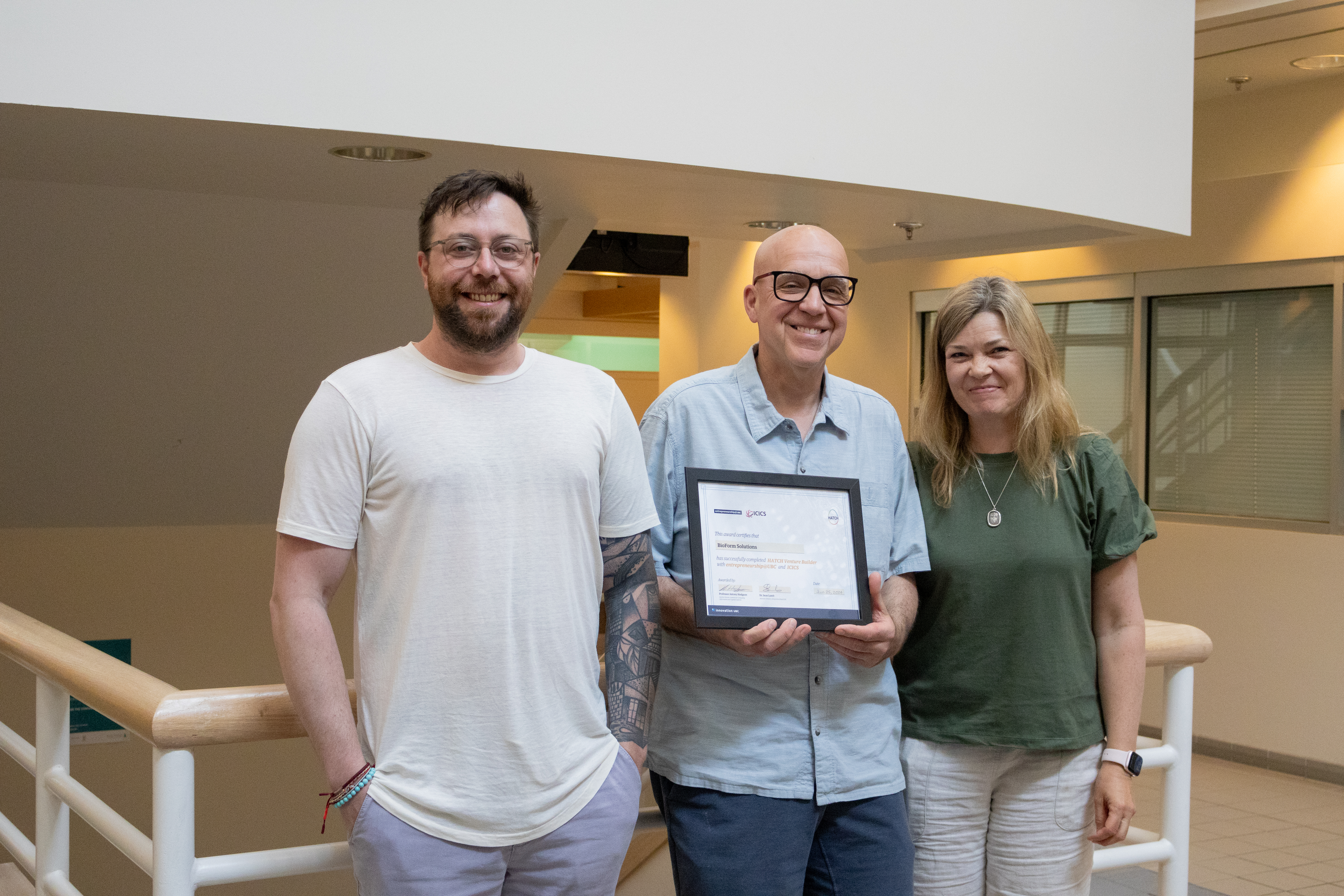 Three people smiling holding an award.