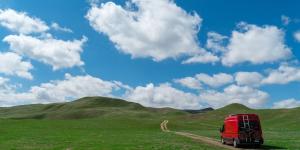 Photo of a red van driving across a green landscape with a sunny blue sky