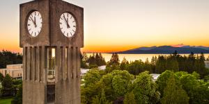 Clocktower with leafy green trees and a sunset over a mountain