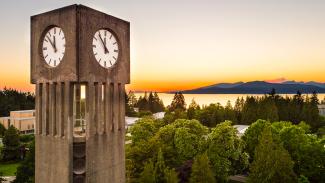 Clocktower with leafy green trees and a sunset over a mountain
